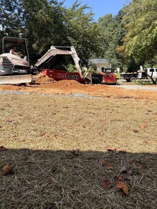 A Bobcat excavator loads dirt into a redbox+ dumpster at a waterproofing service construction site.