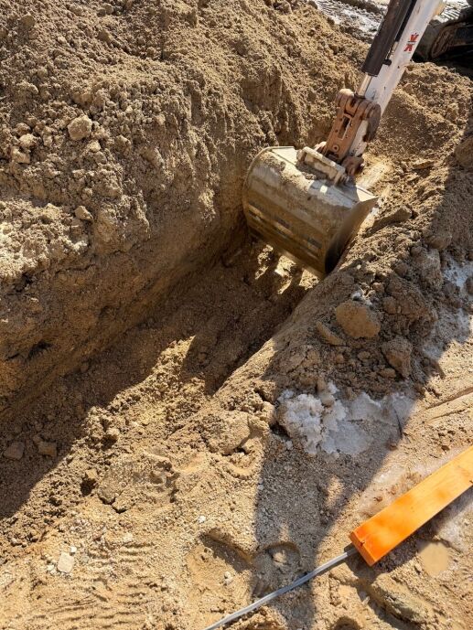 An excavator bucket digging a trench for a waterproofing service in the dirt.